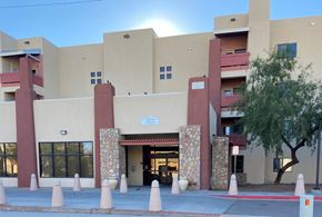 El Paso apartment for rent - The image shows a building with a beige facade and a red entrance, surrounded by a row of trees.