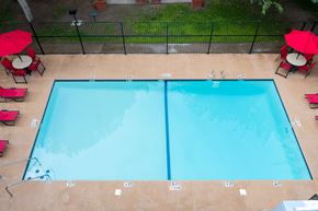 El Paso apartment for rent - A rectangular pool with a blue tint is surrounded by a black fence and has red umbrellas on the side.