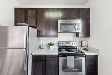 Cayce apartment for rent - A modern kitchen with a stainless steel refrigerator, a stove with an oven, and dark brown cabinets.