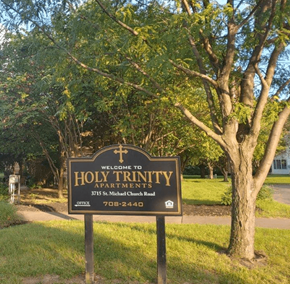 Louisville apartment for rent - a sign for holy trinity apartments in front of a tree