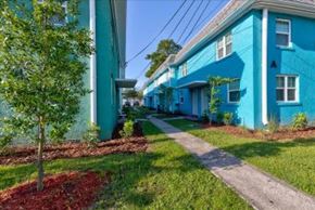 Jacksonville apartment for rent - A tree is planted in a flower bed in front of a blue building.