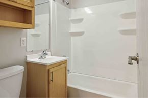 Rock Island apartment for rent - A white sink with a wooden cabinet and a white bathtub with a glass shower door.