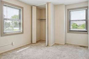 Rock Island apartment for rent - A room with a carpeted floor, two windows with blinds, and a closet with a shelf.