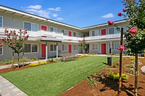 Castro Valley apartment for rent - A building with red doors and windows is surrounded by a green lawn and trees.