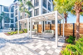 Poolside patio with white pergola and soft seating.