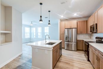 Modern kitchen with island, pendant lighting, stainless steel appliances, and wood-designed flooring.