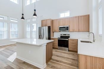 Island kitchen with quartz countertops, stainless steel appliances, and designer plank flooring.