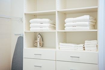 A white closet with shelves and drawers with folded towels and a surfboard