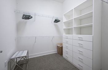 A walk in closet in a room with white walls and shelves and a white bench
