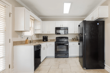 Tuscaloosa apartment for rent - A black refrigerator stands in a kitchen with white cabinets and appliances.