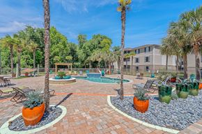 Biloxi apartment for rent - A sunny day at a poolside with a palm tree and a building in the background.