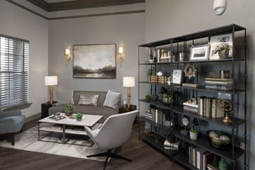 Tuscaloosa apartment for rent - A living room with a grey sofa, a white chair, a coffee table, and a bookshelf with various decorative items.