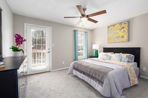 Hoover apartment for rent - A bedroom with patio access, carpet flooring, ceiling fan, and a window at Summerchase at Riverchase in Hoover, Alabama.