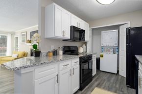 Hoover apartment for rent - A galley-style kitchen with white cabinets, black appliances, granite countertops, and a washer and dryer in a laundry closet at Summerchase at Riverchase in Hoover, Alabama.