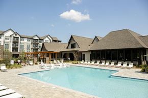 Charlotte apartment for rent - A large swimming pool surrounded by lounge chairs and buildings in the background.