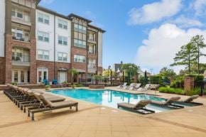 Baton Rouge apartment for rent - A large swimming pool surrounded by lounge chairs in front of a multi-story apartment building.