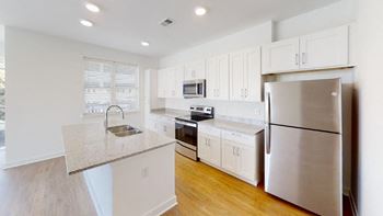 Modern white kitchen with island, wood plank flooring, and stainless steel appliances.