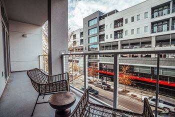 A balcony with a chair and a table overlooking a city street