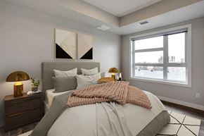 Edmonton apartment for rent - A bedroom with a large bed, a nightstand with a lamp, and a window showing a view of a street.