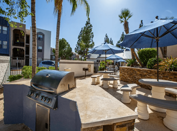 A bbq grill in a courtyard with tables and umbrellas 