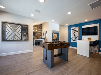 A game room with plank  flooring foosball table, wall scrabble, and seating areas 