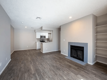 Spacious living room with a fireplace, plank flooring, a kitchen in the background at enclave 