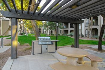 A picnic area with a grill and a table under a pergola.