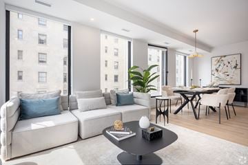 Montreal apartment for rent - A modern living room with a white sofa, a black coffee table, and a dining table with chairs.