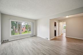 Detroit apartment for rent - A spacious room with wooden floors and a large window overlooking a residential area.