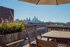 Philadelphia apartment for rent - A wooden table and chairs are set up on a deck with a view of a city skyline.