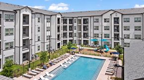 Houston apartment for rent - A large swimming pool surrounded by lounge chairs and umbrellas in front of a multi-story apartment building.