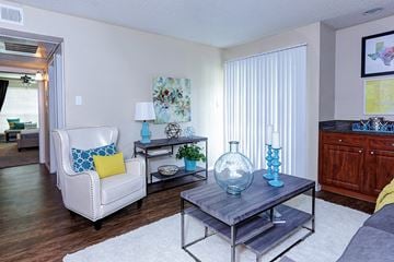 San Antonio apartment for rent - A living room with a white chair and a glass table with a blue vase on it.