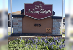 Sweetwater apartment for rent - Mustang Heights sign with a stone pillar and flowers in the foreground.