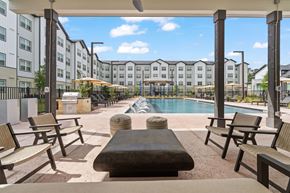 Humble apartment for rent - A pool area with chairs and a table in the foreground and apartment buildings in the background.