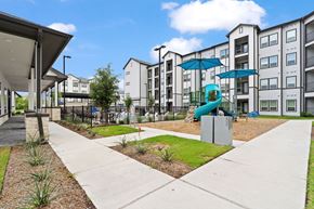 Houston apartment for rent - A modern apartment complex with a playground and a fence.