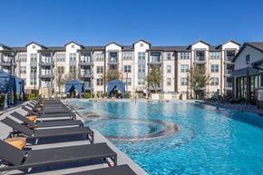 Del Valle apartment for rent - A large swimming pool surrounded by sun loungers in front of apartment buildings. at Enclave on Ross Apartments, Del Valle, TX, 78617