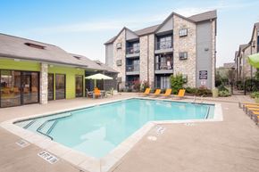 Austin apartment for rent - A pool surrounded by chairs and umbrellas in front of a building.
