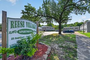 Emporia apartment for rent - A sign for Reese Village Apartments stands in front of a tree and apartment buildings.