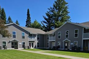 Iron River apartment for rent - A building with a grey facade and a green lawn in front.