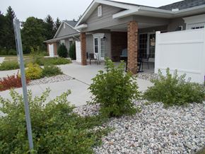 Plainwell apartment for rent - a yard with gravel and bushes in front of a house