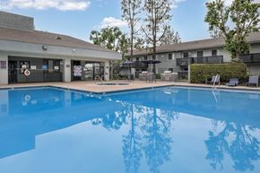 San Bernardino apartment for rent - A large blue swimming pool in front of a building with a tree in the background.
