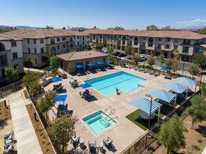 Simi Valley apartment for rent - A large swimming pool surrounded by blue umbrellas and lounge chairs.