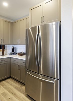 Clovis townhouse for rent - A stainless steel refrigerator stands in a kitchen with wooden floors and beige cabinets.