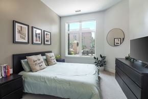 Downers Grove apartment for rent - A bedroom with a bed, nightstand, and a window with a view of a building outside.