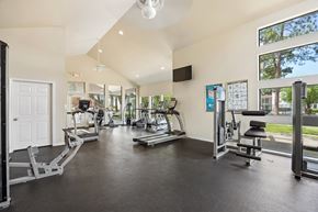 Tyler apartment for rent - A spacious gym with a variety of equipment and a view of the outdoors through large windows.