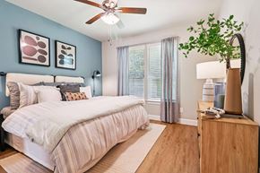 Conroe apartment for rent - A bedroom with a bed, a ceiling fan, and a nightstand with a plant on it.