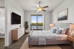 Orlando apartment for rent - A bedroom with a large bed, a flat screen TV, and a balcony with a view of trees.