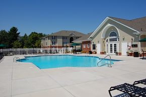 Greensboro apartment for rent - A large swimming pool in front of a building with a white fence and trees in the background.