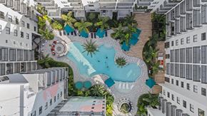 Doral apartment for rent - A pool surrounded by palm trees and a white building.