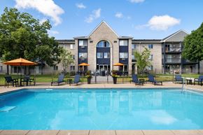 Coon Rapids apartment for rent - A swimming pool in front of a building with a patio and chairs.